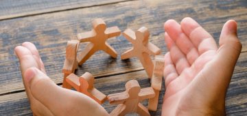 Business success concept on wooden background high angle view. hands protecting wooden figures of people.